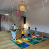 TOCKI Kinderyogamatten – Ein Kind in einem fröhlichen Yoga-Gruppenkurs, das auf der rutschfesten Yogamatte mit einem lustigen Maus-Motiv übt.